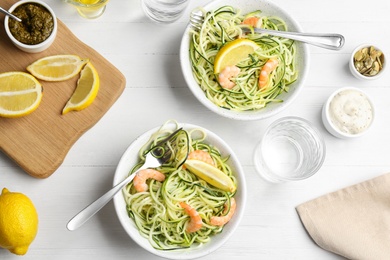 Photo of Delicious zucchini pasta with shrimps and lemon served on white wooden table, flat lay