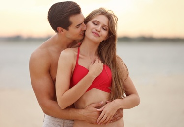 Happy young couple spending time together on sea beach at sunset