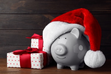 Piggy bank with Santa hat and gift boxes on wooden table