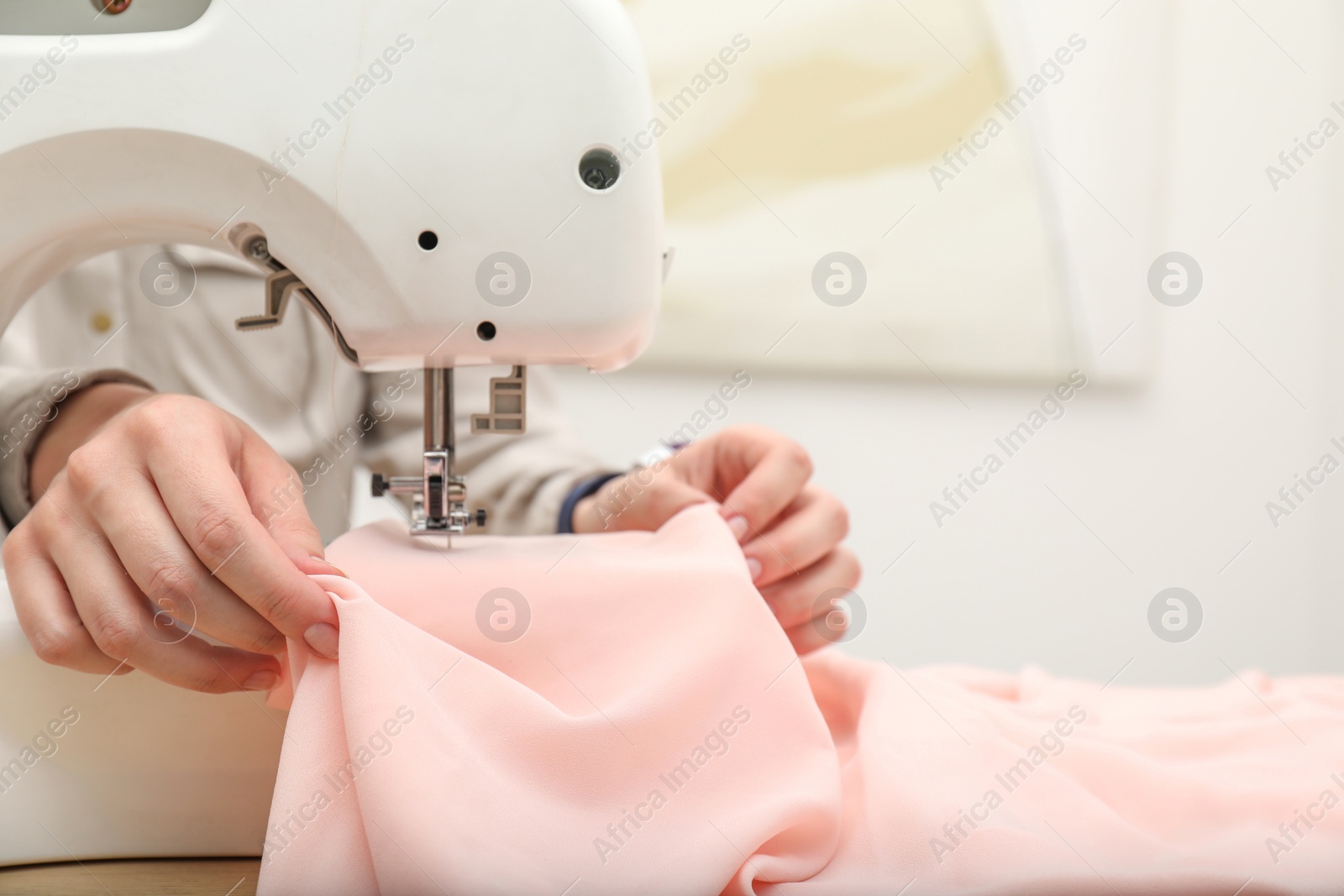 Photo of Seamstress working with sewing machine at table indoors, closeup