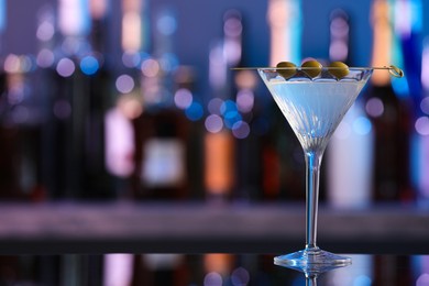 Photo of Martini glass with cocktail and olives on counter in bar. Space for text