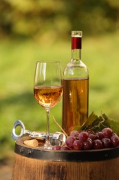 Photo of Delicious wine and ripe grapes on wooden barrel outdoors