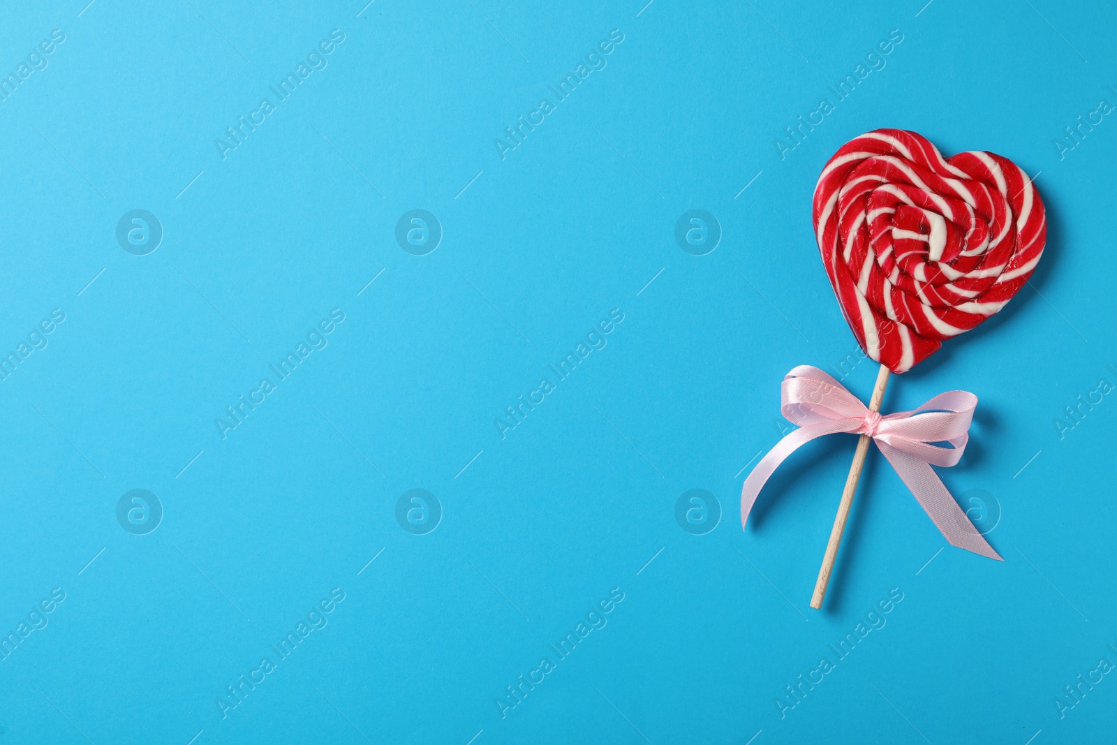 Photo of Sweet heart shaped lollipop on light blue background, top view with space for text. Valentine's day celebration