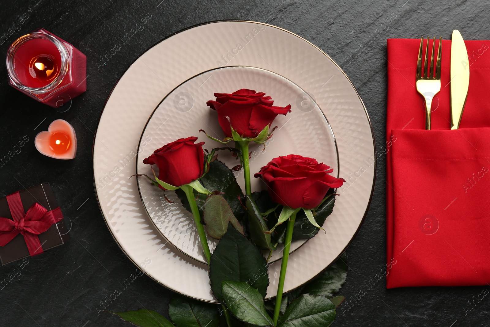 Photo of Place setting with candles, gift box and roses on grey textured table, flat lay. Romantic dinner