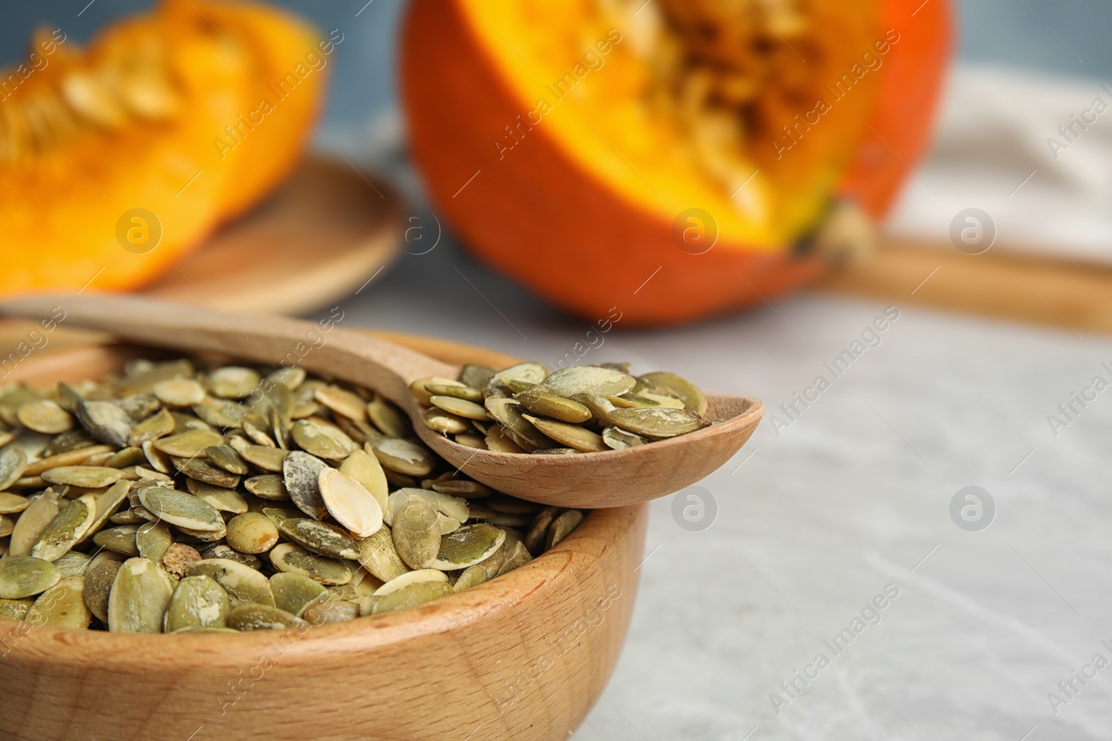 Photo of Bowl and spoon of raw pumpkin seeds on light grey table, closeup. Space for text