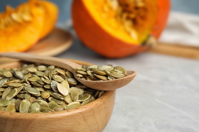 Photo of Bowl and spoon of raw pumpkin seeds on light grey table, closeup. Space for text