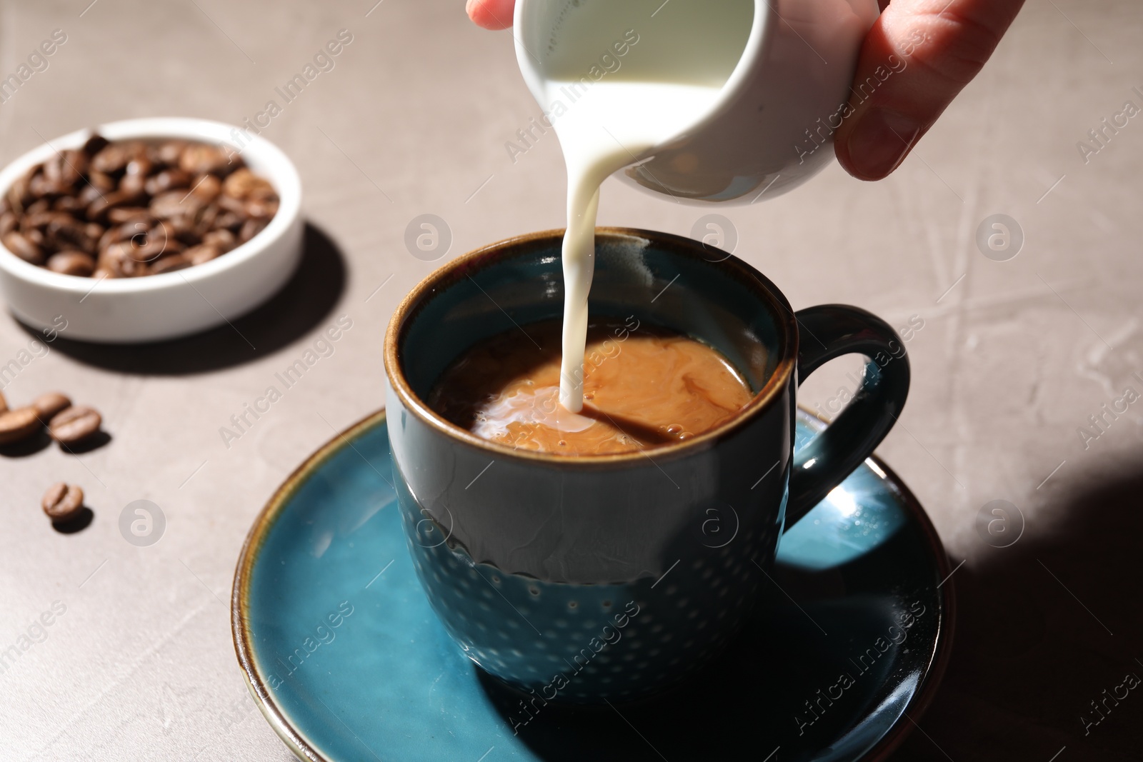 Photo of Woman pouring milk into cup with aromatic coffee at light table, closeup