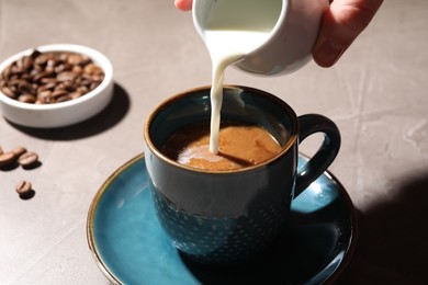 Photo of Woman pouring milk into cup with aromatic coffee at light table, closeup