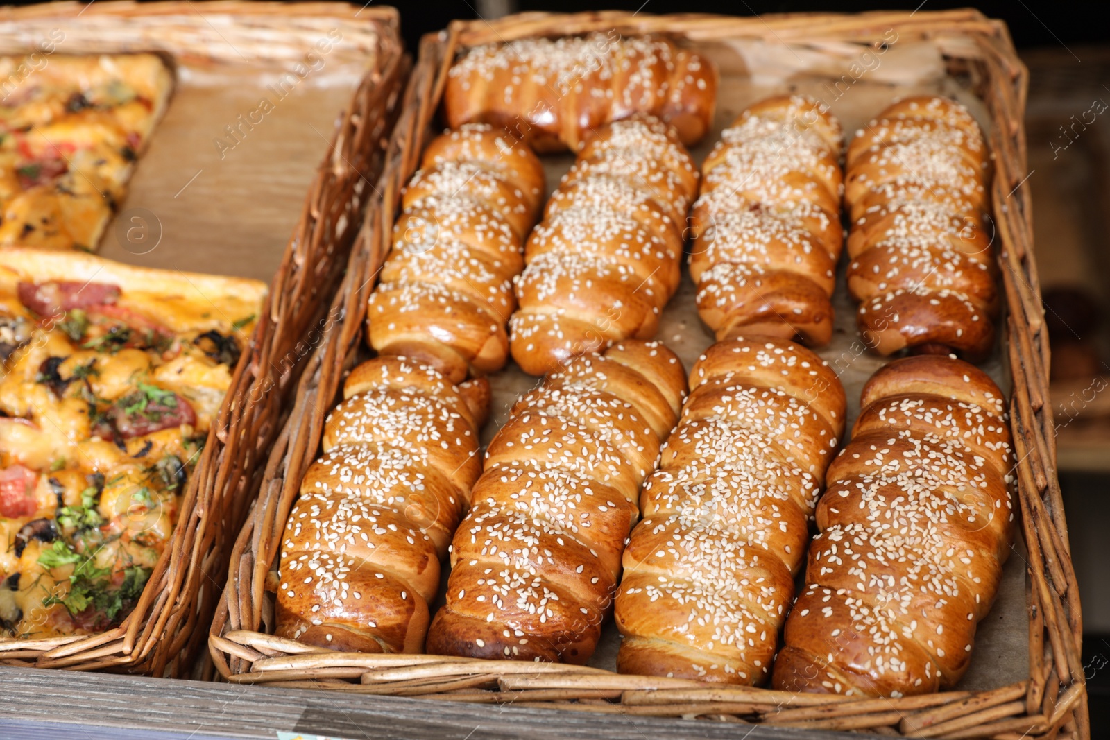 Photo of Wicker trays with fresh buns and pizza in bakery store