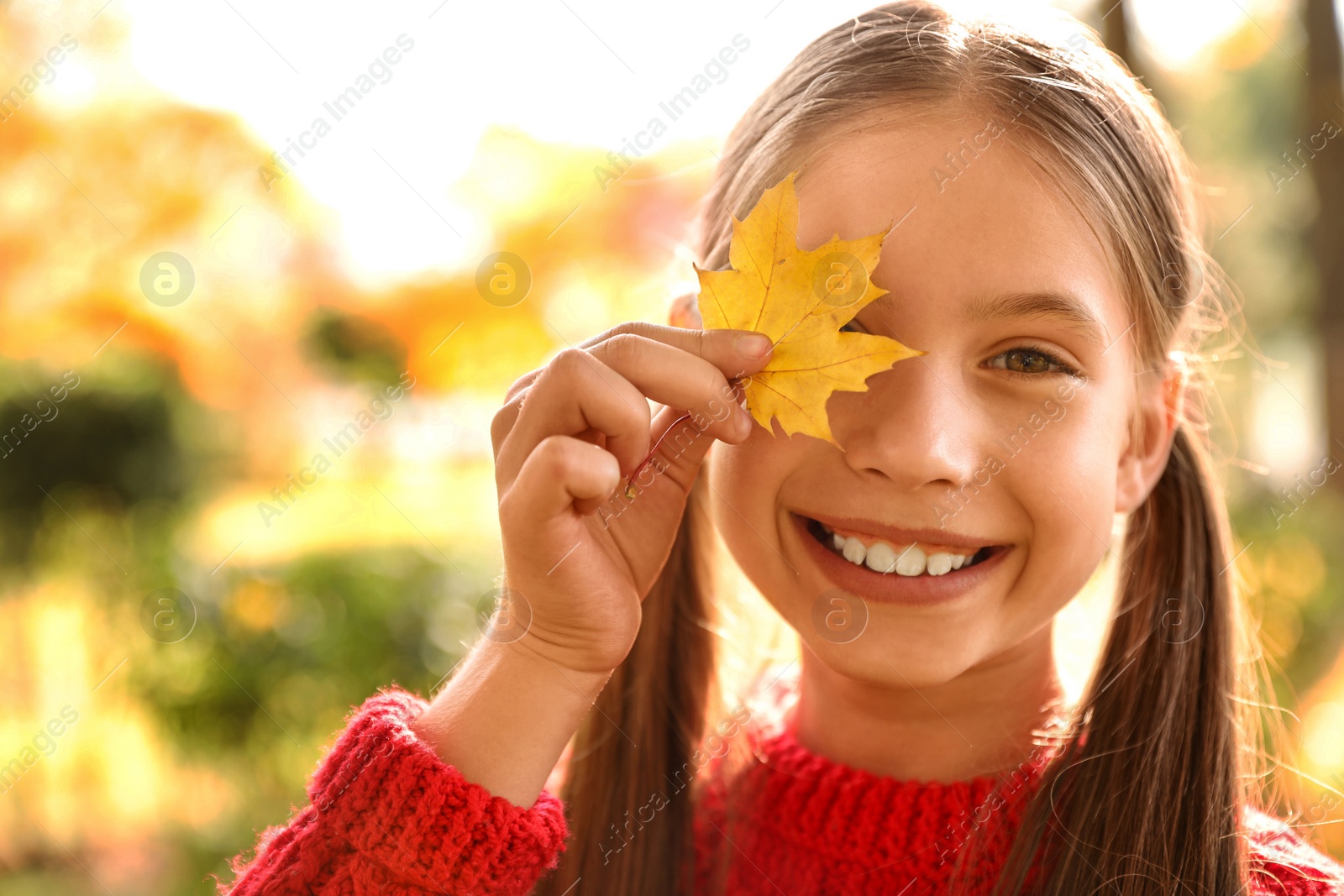 Photo of Happy girl with yellow leaf in sunny park. Autumn walk