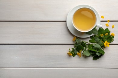 Photo of Cup of aromatic celandine tea and flowers on white wooden table, flat lay. Space for text