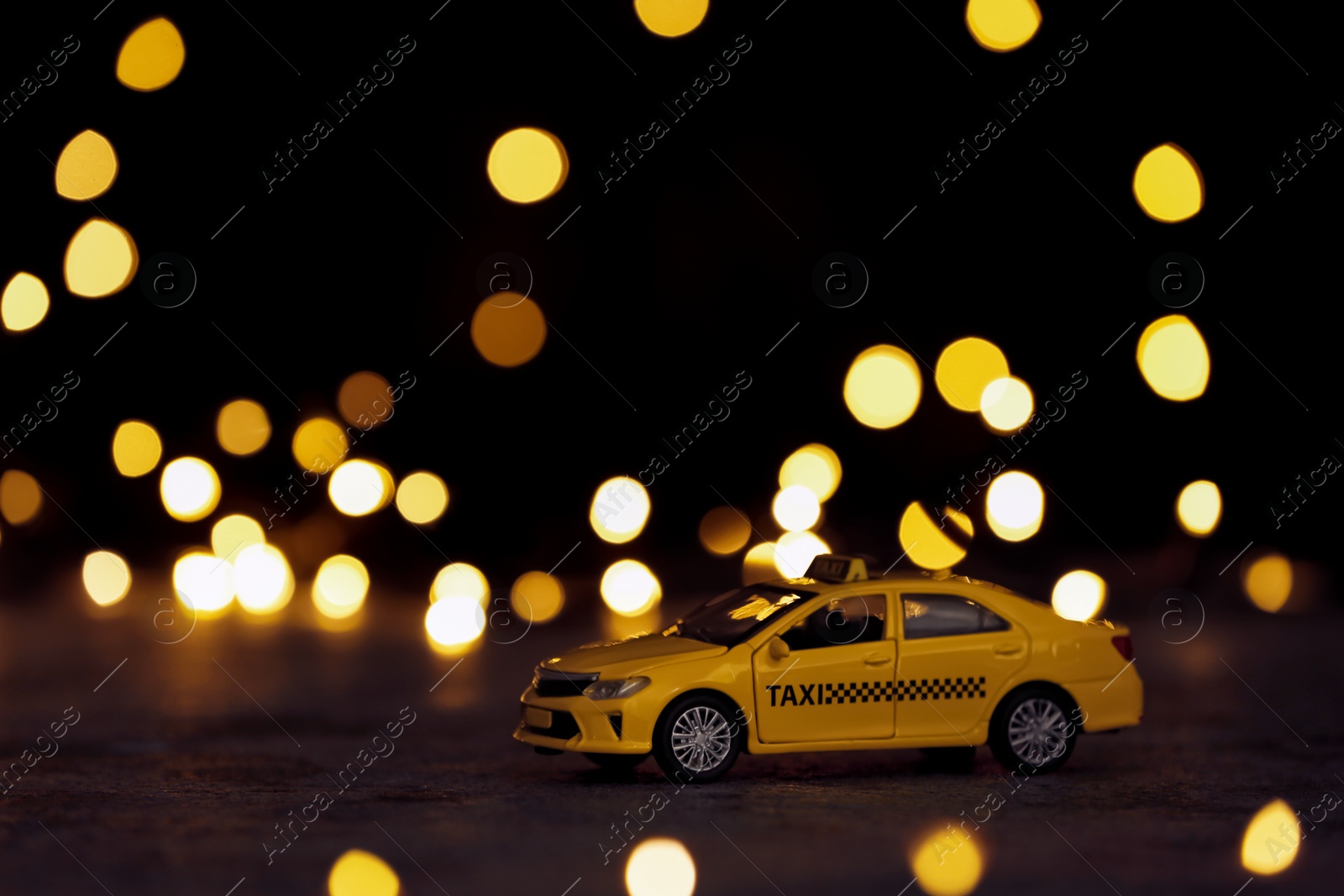 Photo of Yellow taxi car model on table against festive lights. Bokeh effect