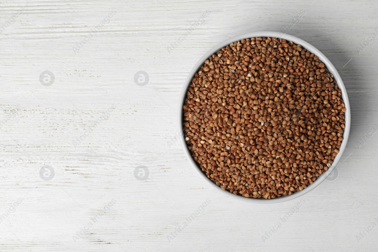 Photo of Uncooked buckwheat in bowl on wooden table, top view. Space for text