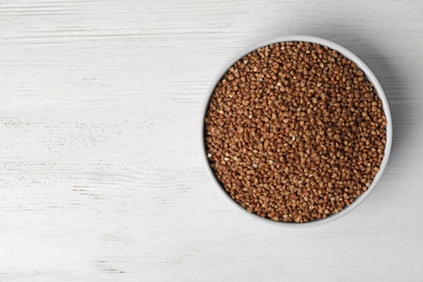 Uncooked buckwheat in bowl on wooden table, top view. Space for text