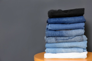 Photo of Stack of different jeans on  table against gray background. Space for text