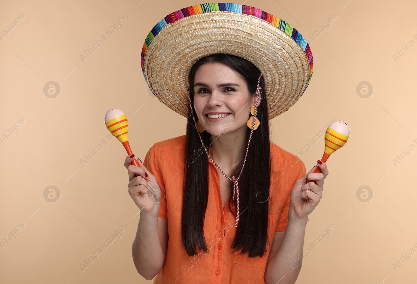 Photo of Young woman in Mexican sombrero hat with maracas on beige background