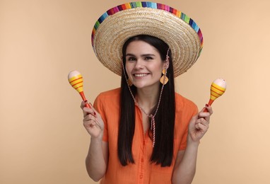 Photo of Young woman in Mexican sombrero hat with maracas on beige background