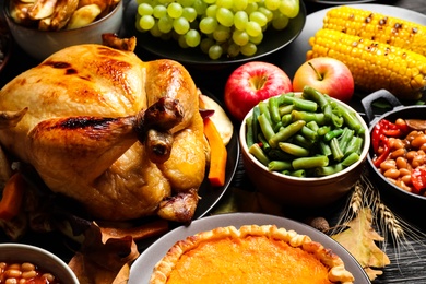 Photo of Traditional Thanksgiving day feast with delicious cooked turkey and other seasonal dishes served on black wooden table, closeup