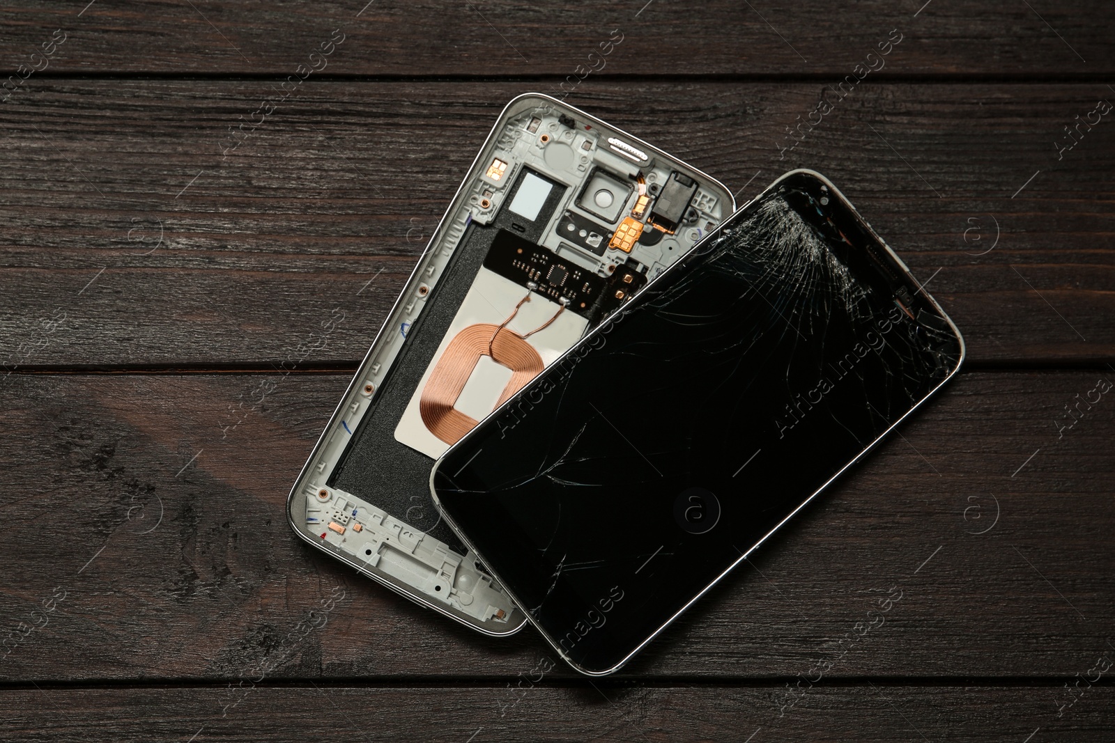 Photo of Damaged smartphone on dark wooden table, flat lay. Device repairing