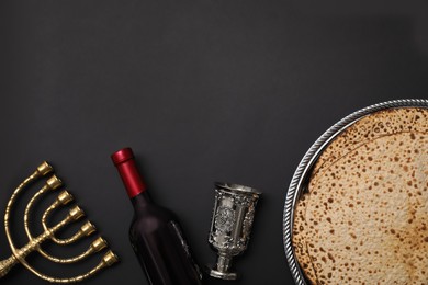 Photo of Tasty matzos, menorah and wine on black background, flat lay with space for text. Passover (Pesach) celebration