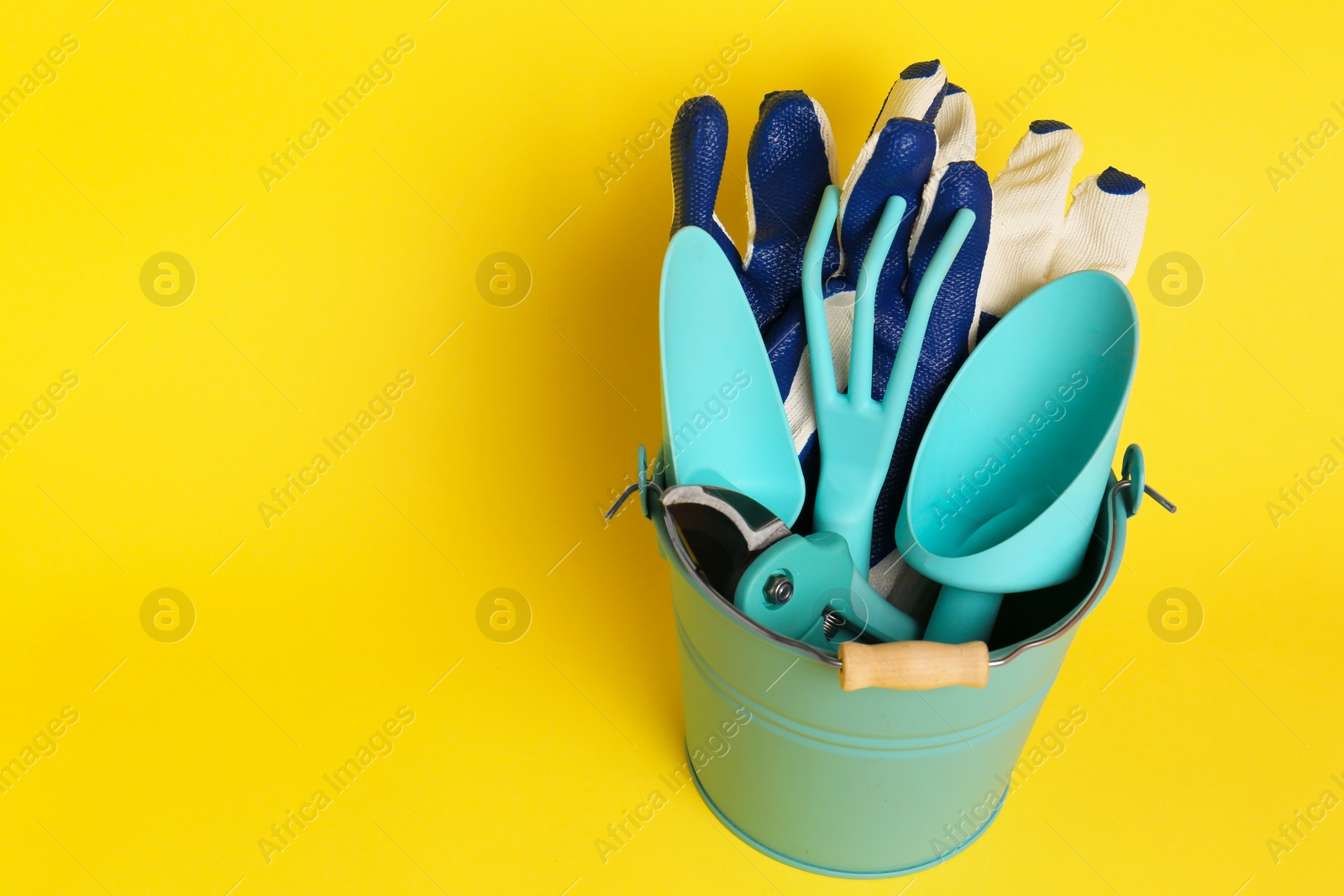 Photo of Bucket with gardening gloves and tools on yellow background. Space for text