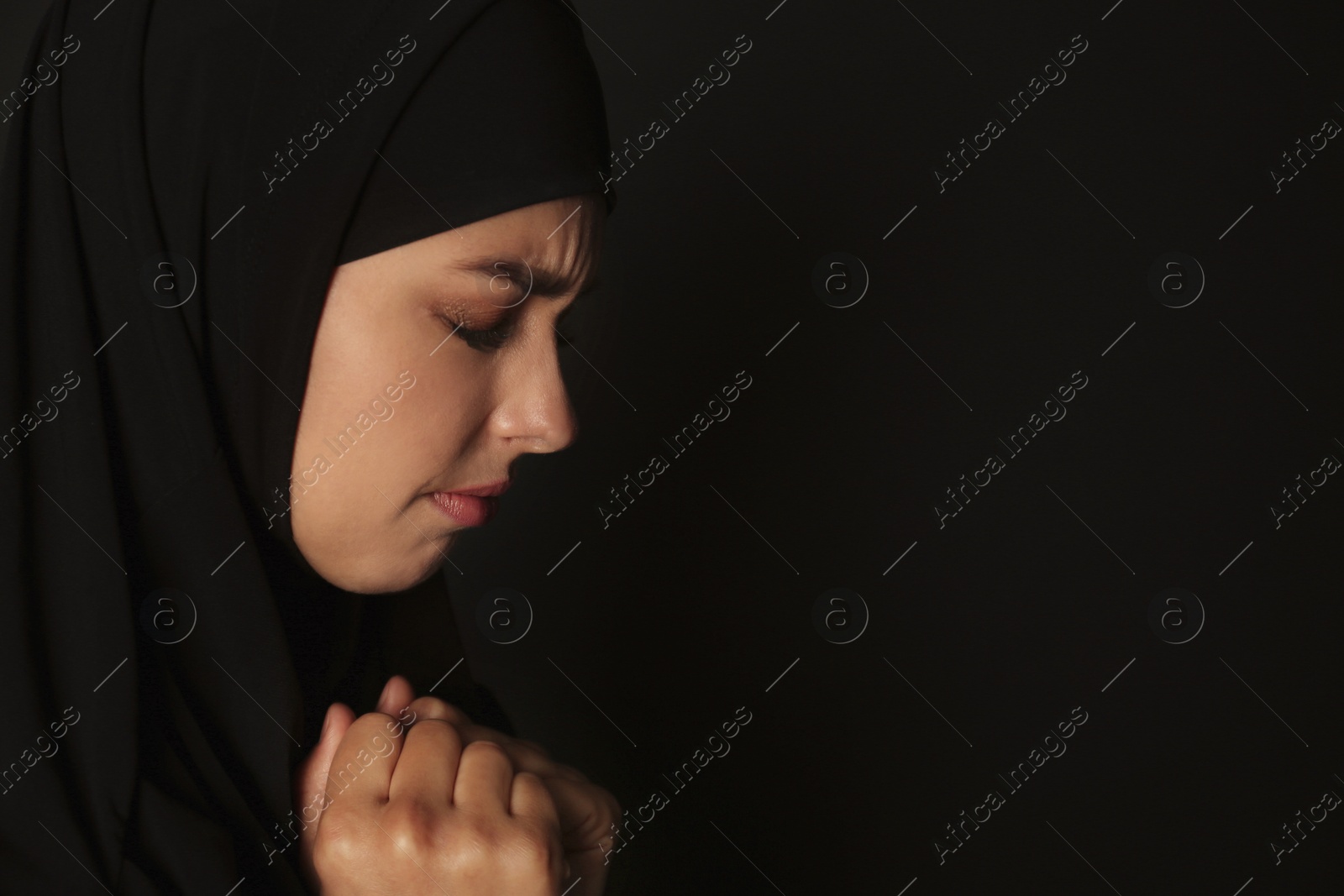 Photo of Portrait of sad Muslim woman in hijab  praying on dark background. Space for text