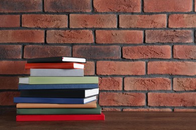 Photo of Stack of hardcover books on wooden table near brick wall. Space for text