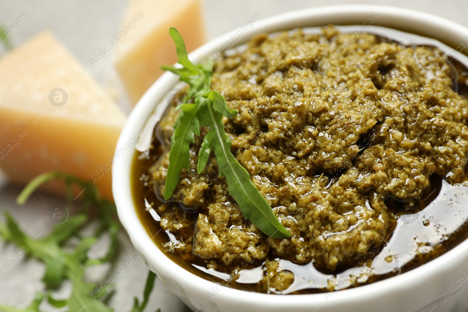 Photo of Bowl of tasty arugula pesto on table, closeup