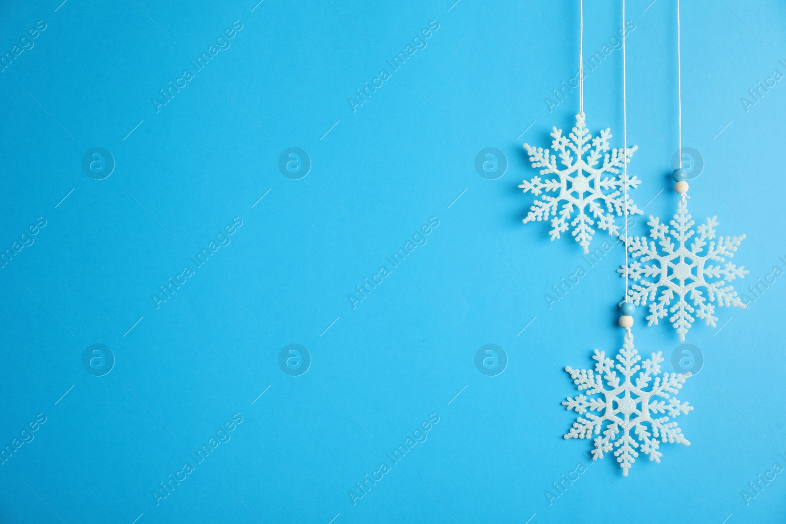 Photo of Beautiful decorative snowflakes hanging on light blue background, space for text