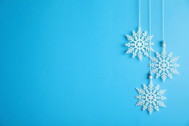 Photo of Beautiful decorative snowflakes hanging on light blue background, space for text