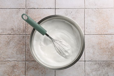 Photo of Bowl and whisk with whipped cream on tiled table, top view