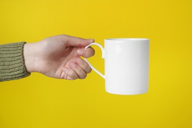 Woman holding white mug on yellow background, closeup