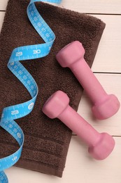 Dumbbells, measuring tape and towel on white wooden table, flat lay