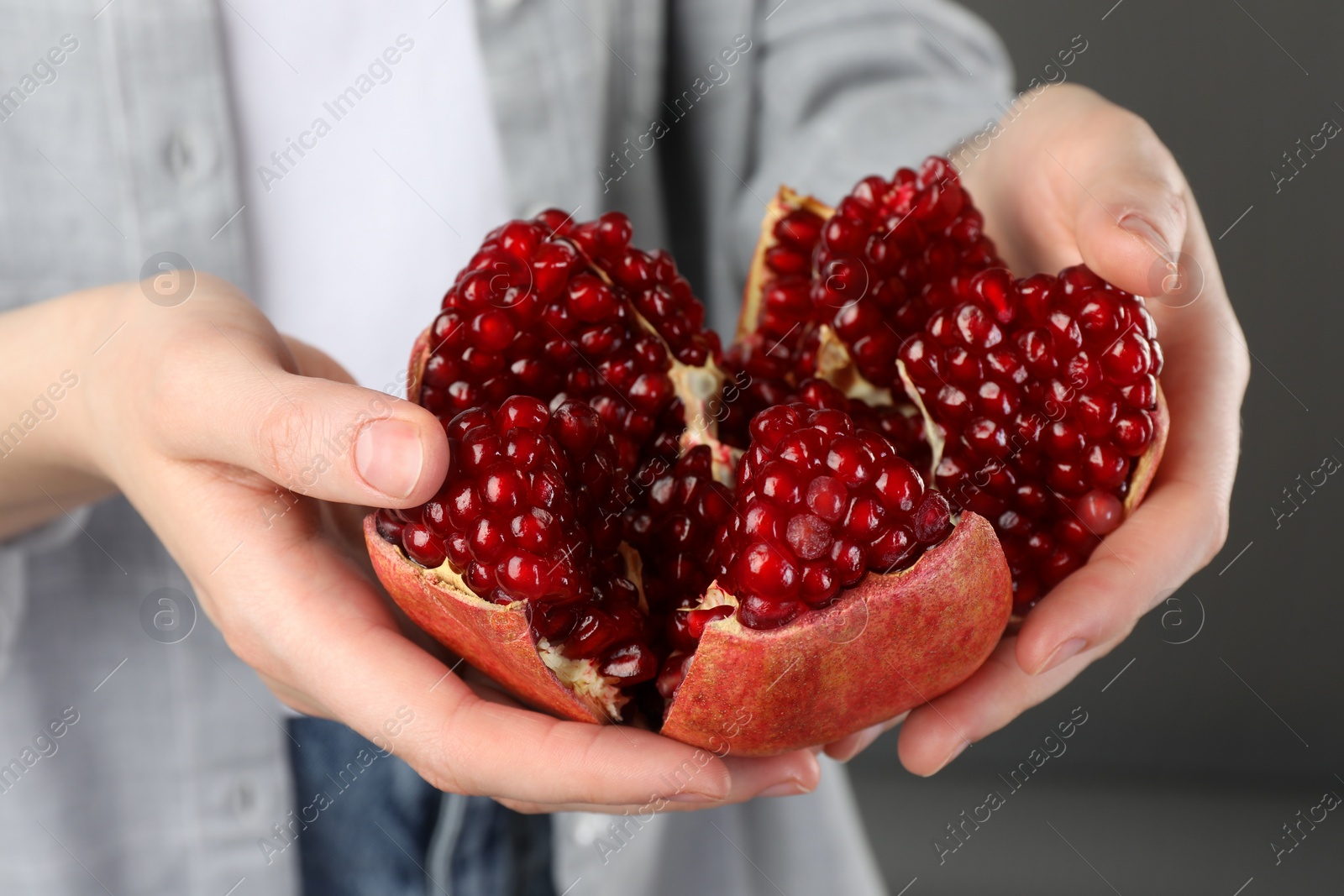 Photo of Woman holding fresh pomegranate on grey background, closeup