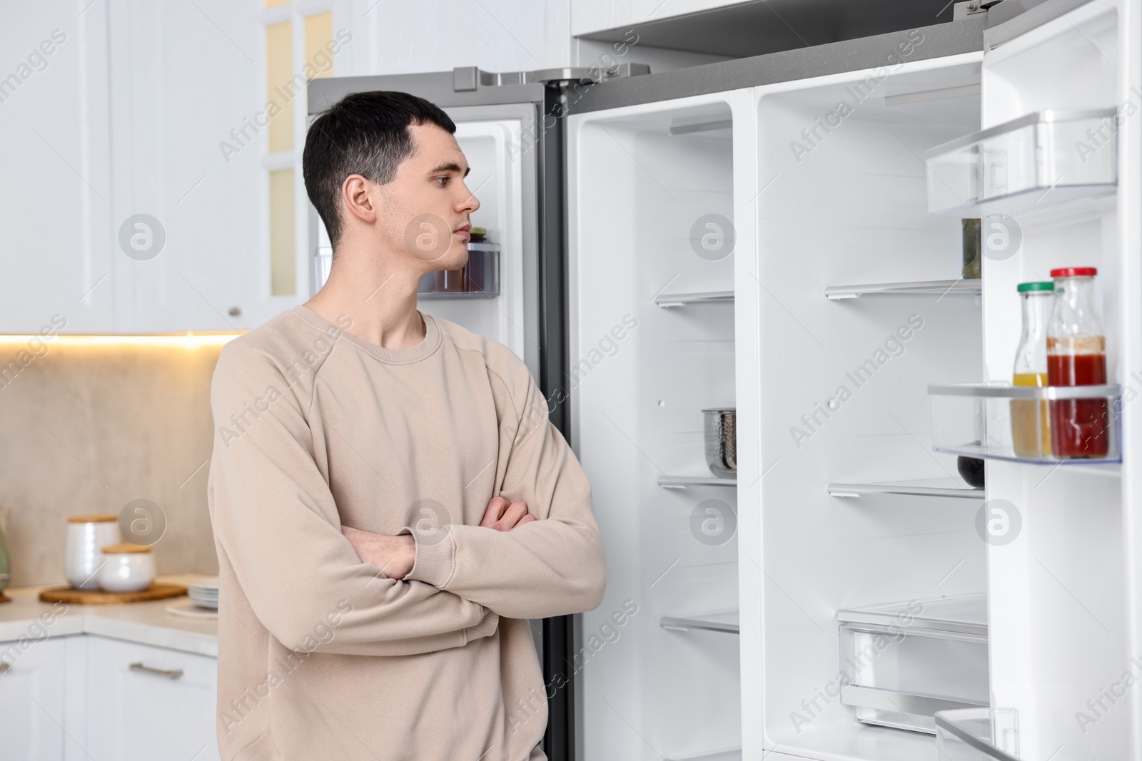 Photo of Upset man near empty refrigerator in kitchen