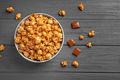 Photo of Delicious popcorn with caramel in bowl and candies on wooden background, top view