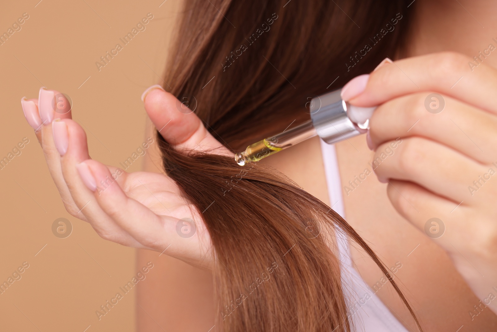 Photo of Woman applying serum onto hair on beige background, closeup