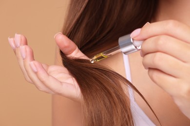 Photo of Woman applying serum onto hair on beige background, closeup