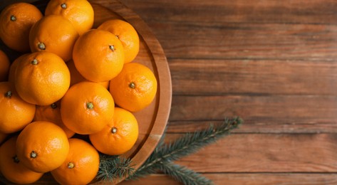 Photo of Stand with delicious ripe tangerines and fir twigs on wooden table, top view. Space for text