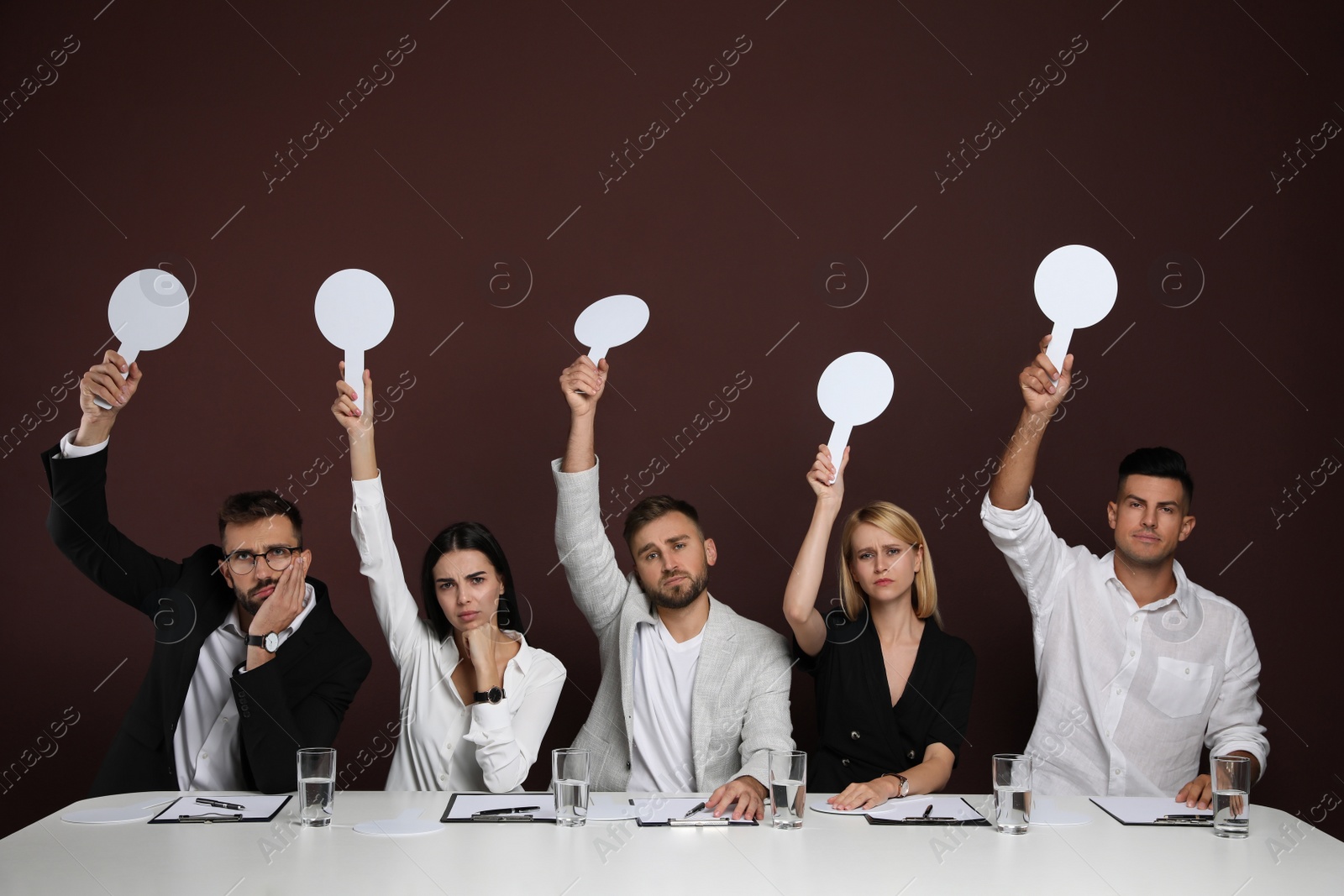 Photo of Panel of disappointed judges holding blank score signs at table on brown background. Space for text