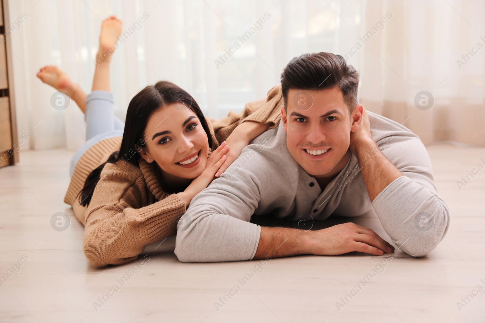 Photo of Happy couple lying on warm floor at home. Heating system