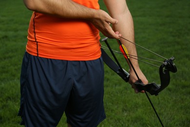 Photo of Man with bow and arrow practicing archery on green grass, closeup
