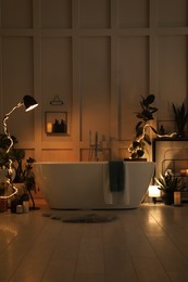 Photo of Stylish bathroom interior with houseplants and string lights. Home design