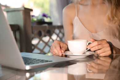 Woman with cup of coffee and laptop on cafe terrace in morning, closeup