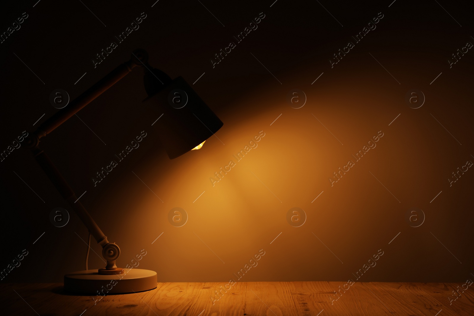 Photo of Stylish modern desk lamp on wooden table at night, space for text