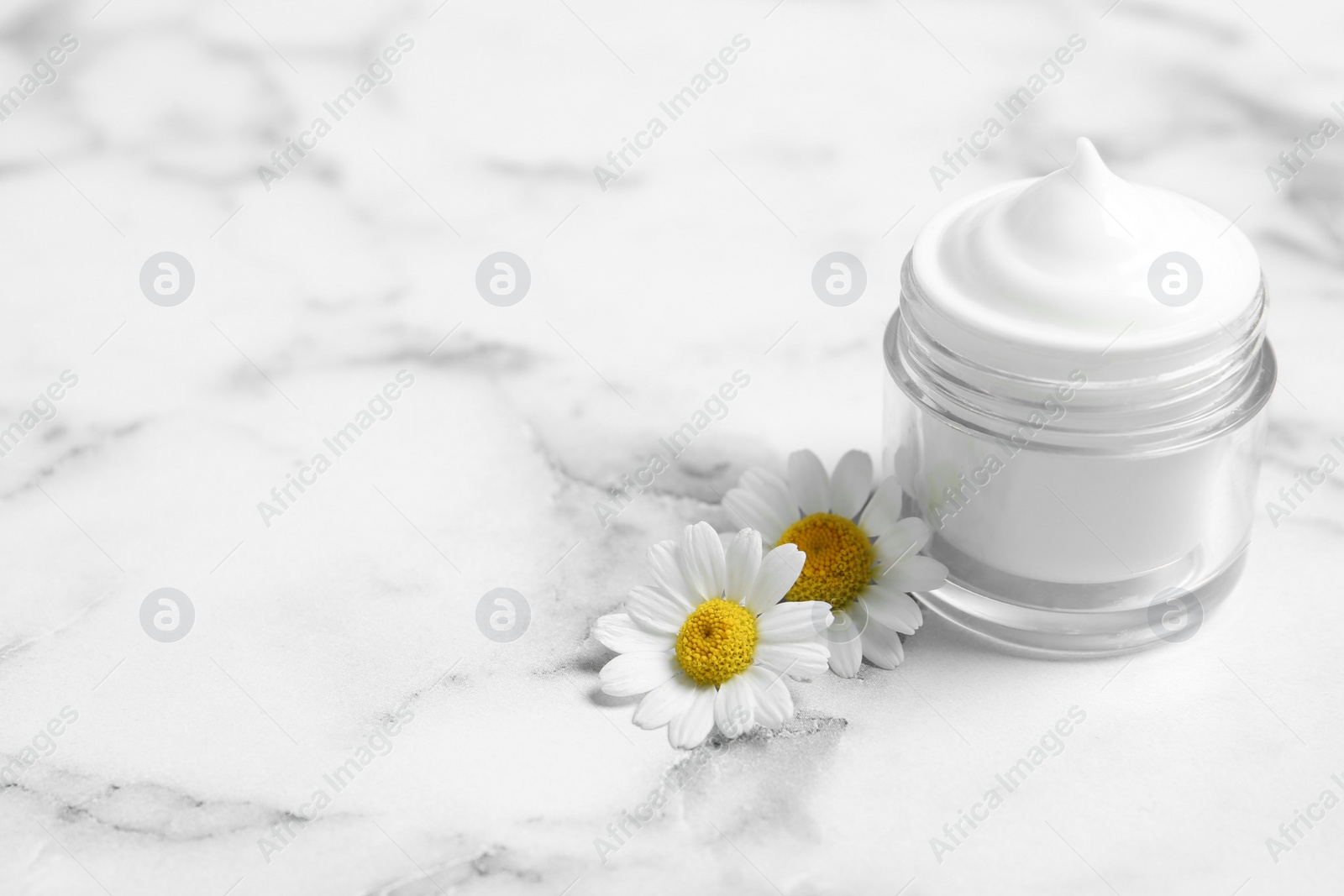 Photo of Chamomile flowers and jar of cream on white marble table. Space for text