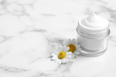 Chamomile flowers and jar of cream on white marble table. Space for text