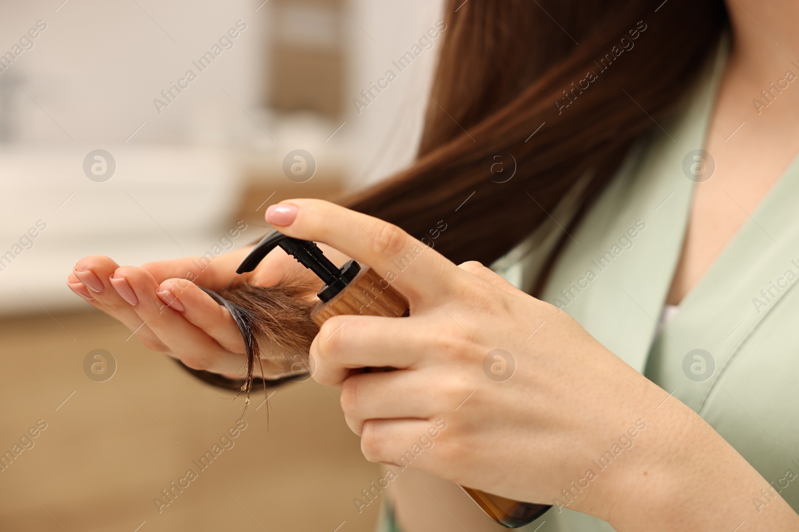 Photo of Woman applying oil hair mask indoors, closeup