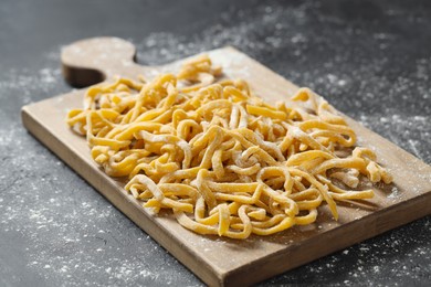 Photo of Board with homemade pasta and flour on dark table