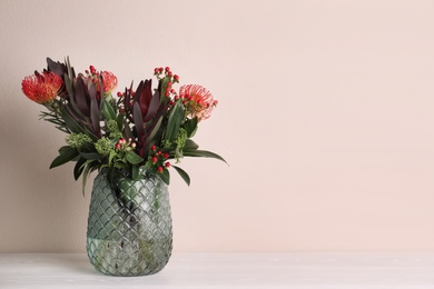 Photo of Vase with bouquet of beautiful protea flowers on white wooden table near beige wall. Space for text